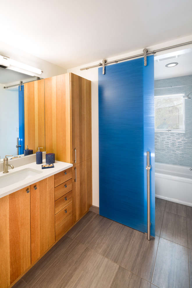Design ideas for a mid-sized contemporary kids bathroom in Denver with flat-panel cabinets, light wood cabinets, an alcove tub, a shower/bathtub combo, a two-piece toilet, blue tile, porcelain tile, white walls, porcelain floors, an undermount sink, quartzite benchtops and a shower curtain.