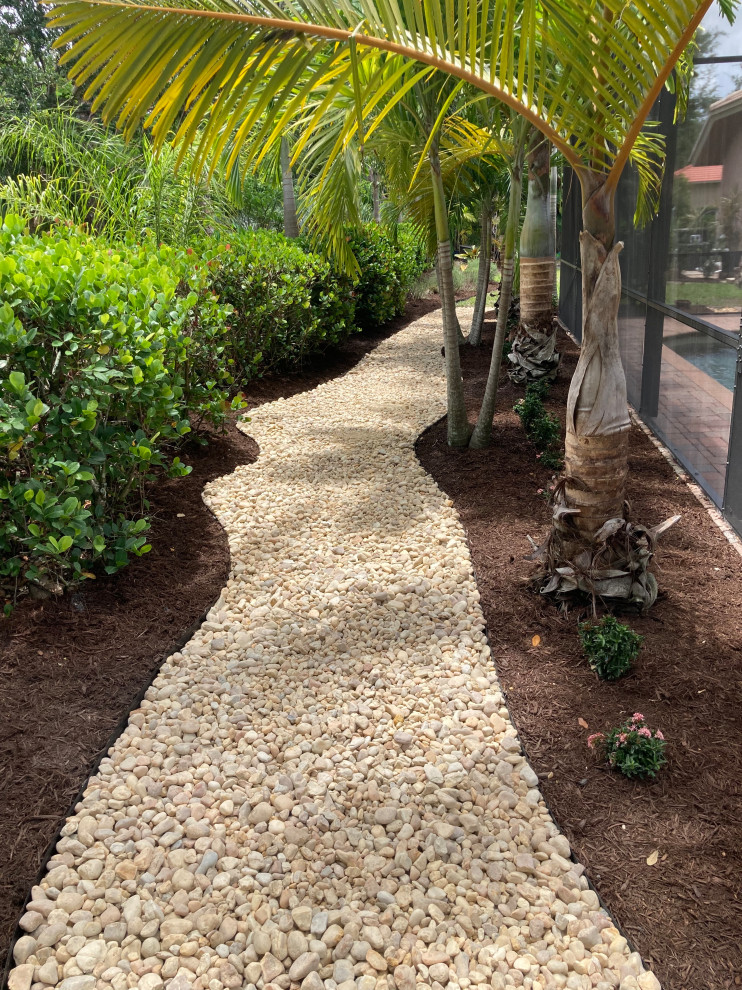 This is an example of an expansive tropical side yard full sun xeriscape for summer in Miami with with rock feature and river rock.
