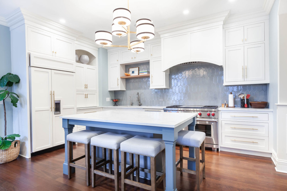 This is an example of a large transitional l-shaped eat-in kitchen in Chicago with an undermount sink, shaker cabinets, white cabinets, quartz benchtops, grey splashback, ceramic splashback, stainless steel appliances, medium hardwood floors, with island, brown floor and white benchtop.