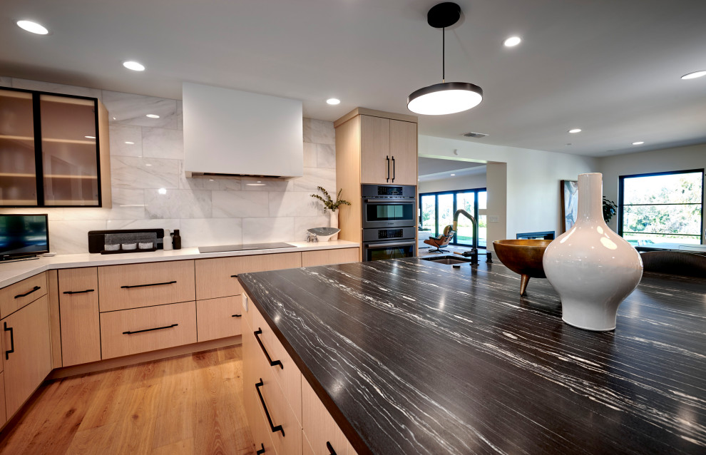 Inspiration for a large modern u-shaped light wood floor and brown floor open concept kitchen remodel in Denver with an undermount sink, flat-panel cabinets, light wood cabinets, quartz countertops, white backsplash, marble backsplash, stainless steel appliances, an island and black countertops