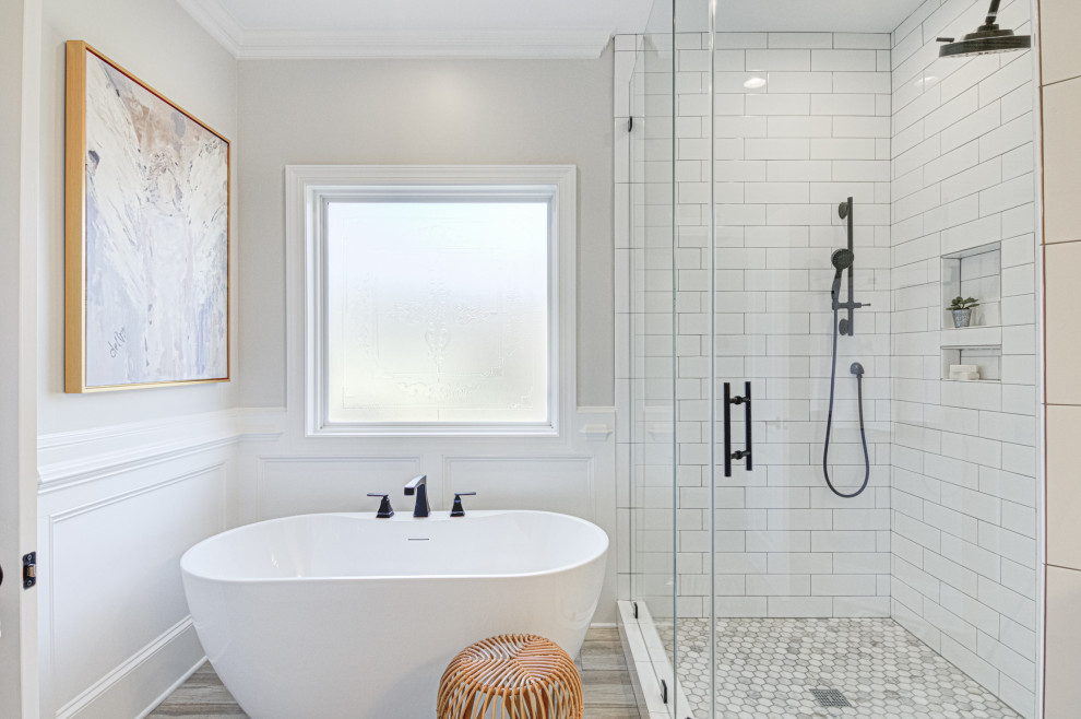 Пример оригинального дизайна: главная ванная комната среднего размера в стиле модернизм с белыми фасадами, отдельно стоящей ванной, угловым душем, раздельным унитазом, белой плиткой, керамической плиткой, серыми стенами, полом из плитки под дерево, врезной раковиной, столешницей из искусственного кварца, коричневым полом, душем с распашными дверями, белой столешницей, тумбой под две раковины, встроенной тумбой и панелями на стенах