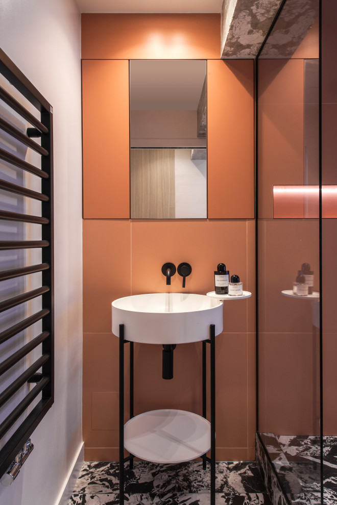 This is an example of a medium sized contemporary ensuite bathroom in Paris with open cabinets, white cabinets, a walk-in shower, a wall mounted toilet, orange tiles, ceramic tiles, orange walls, marble flooring, a pedestal sink, solid surface worktops, black floors, a hinged door, white worktops, a wall niche, a single sink and a freestanding vanity unit.
