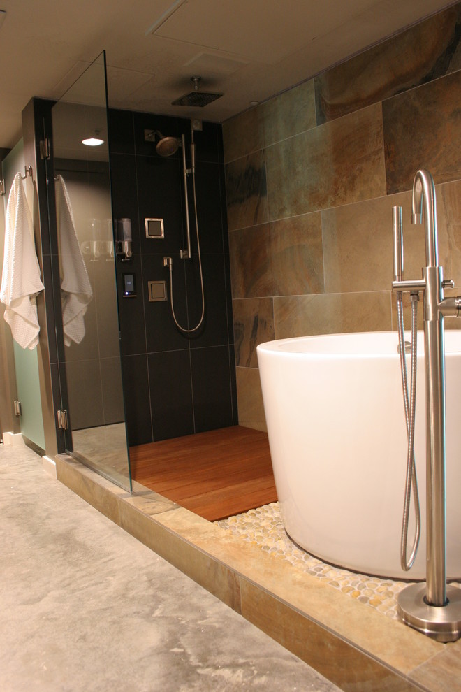 This is an example of a small transitional master bathroom in Houston with flat-panel cabinets, medium wood cabinets, a japanese tub, an open shower, a bidet, black tile, stone tile, grey walls, concrete floors, an integrated sink, quartzite benchtops, grey floor, a hinged shower door and grey benchtops.
