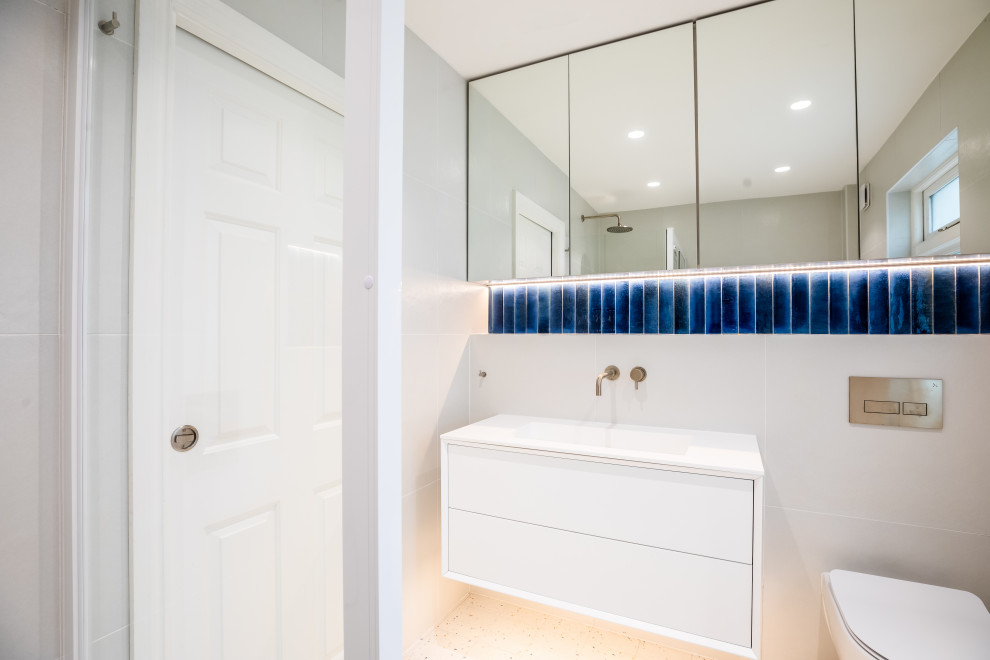 Small modern kids bathroom in London with glass-front cabinets, a freestanding tub, a corner shower, a wall-mount toilet, white tile, porcelain tile, porcelain floors, an integrated sink, soapstone benchtops, a sliding shower screen, white benchtops, a single vanity and a floating vanity.
