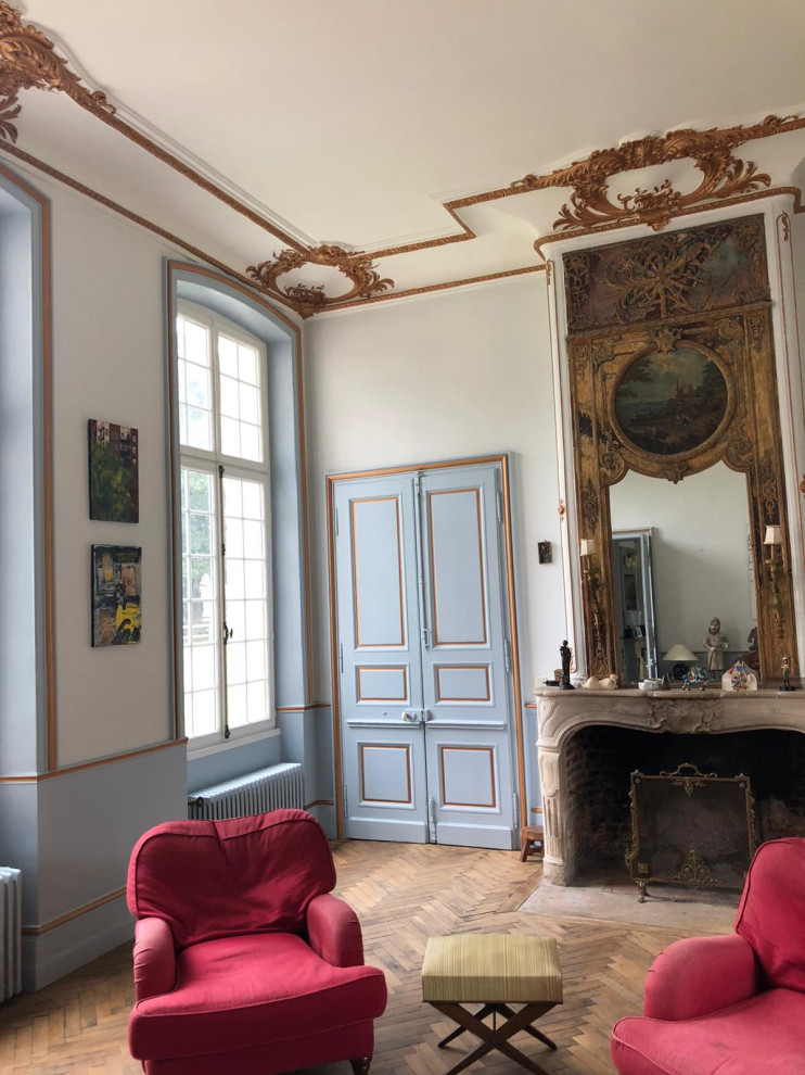 Пример оригинального дизайна: большая гостиная комната в стиле неоклассика (современная классика) с синими стенами, светлым паркетным полом, стандартным камином, фасадом камина из дерева, сводчатым потолком и панелями на стенах