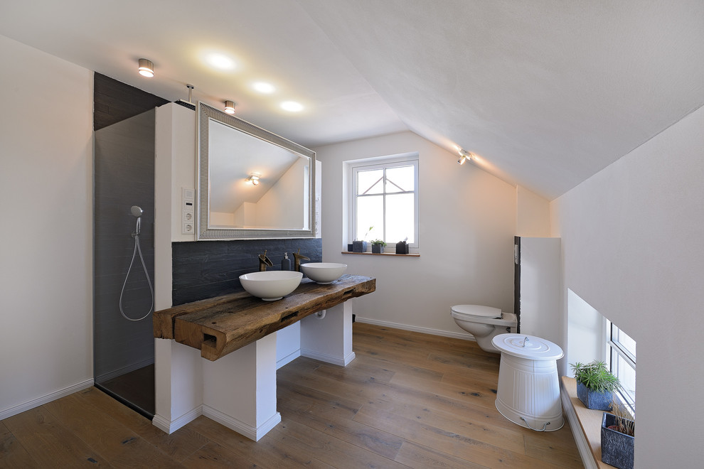 Mid-sized scandinavian 3/4 bathroom in Frankfurt with a curbless shower, a wall-mount toilet, black tile, white walls, medium hardwood floors, a vessel sink and wood benchtops.
