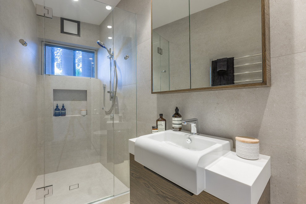 This is an example of a medium sized contemporary shower room bathroom in Auckland with flat-panel cabinets, dark wood cabinets, an alcove shower, a one-piece toilet, beige tiles, ceramic tiles, beige walls, ceramic flooring, a wall-mounted sink, wooden worktops, beige floors, a hinged door, brown worktops, a single sink and a built in vanity unit.