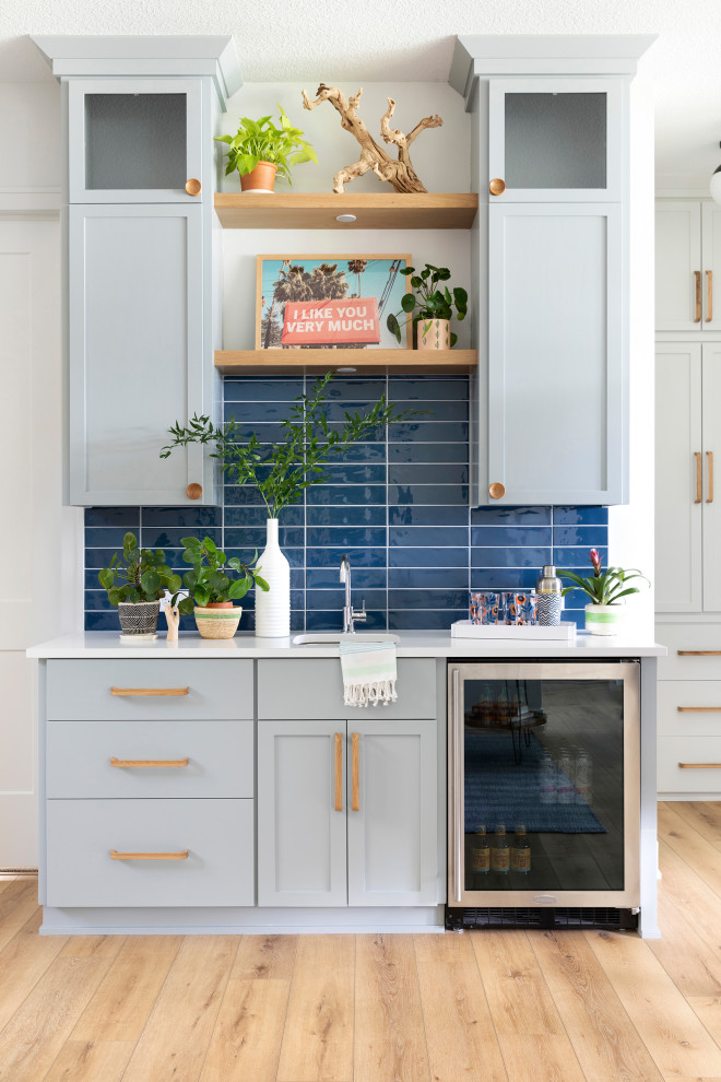This is an example of a mid-sized transitional single-wall wet bar in Minneapolis with an undermount sink, flat-panel cabinets, grey cabinets, quartz benchtops, blue splashback, ceramic splashback, light hardwood floors, beige floor and white benchtop.