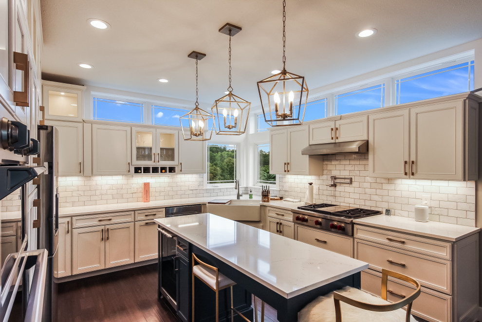 Large transitional u-shaped dark wood floor and brown floor kitchen photo with a farmhouse sink, recessed-panel cabinets, white cabinets, white backsplash, subway tile backsplash, stainless steel appliances, an island and white countertops