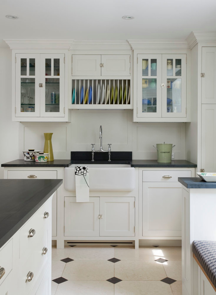 This is an example of a mid-sized transitional separate kitchen in New York with a farmhouse sink, glass-front cabinets, white cabinets, soapstone benchtops, white splashback, with island and limestone floors.