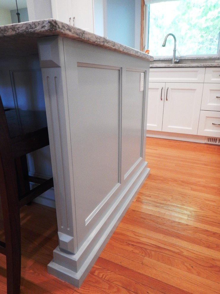 Inspiration for a large transitional l-shaped light wood floor eat-in kitchen remodel with an undermount sink, recessed-panel cabinets, white cabinets, quartz countertops, gray backsplash, stone tile backsplash, stainless steel appliances and an island