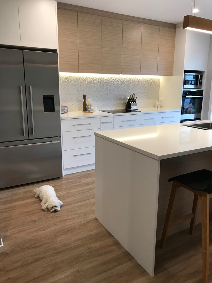 This is an example of a large scandinavian galley separate kitchen in Christchurch with a double-bowl sink, flat-panel cabinets, white cabinets, quartz benchtops, grey splashback, porcelain splashback, stainless steel appliances, with island, brown floor and vinyl floors.