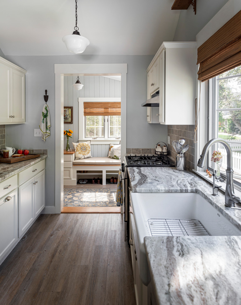 This is an example of a beach style kitchen in Providence with a farmhouse sink, recessed-panel cabinets, white cabinets, quartzite benchtops, limestone splashback and stainless steel appliances.