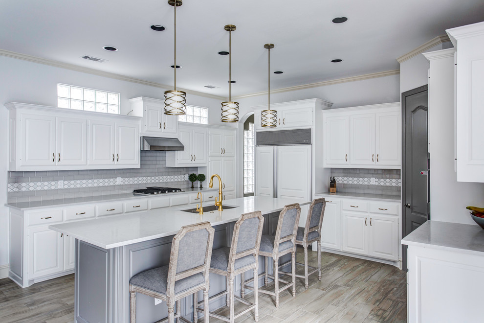 This is an example of a large transitional u-shaped eat-in kitchen in Dallas with an undermount sink, raised-panel cabinets, white cabinets, quartz benchtops, grey splashback, subway tile splashback, porcelain floors, with island, beige floor and white benchtop.