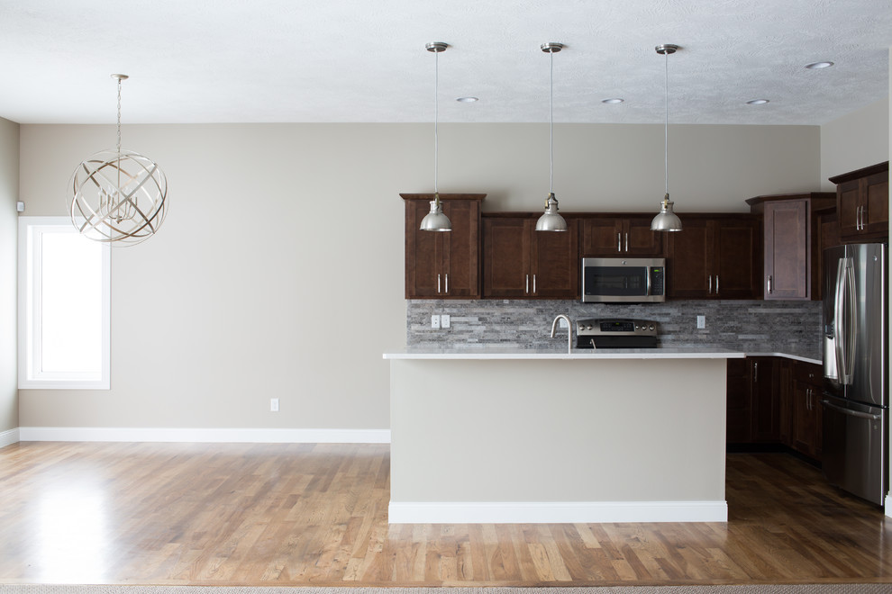 Mid-sized transitional l-shaped dark wood floor enclosed kitchen photo with a double-bowl sink, shaker cabinets, dark wood cabinets, quartz countertops, gray backsplash, stone tile backsplash, stainless steel appliances and an island