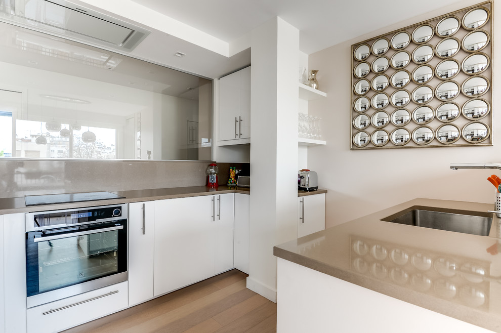 Photo of a mid-sized contemporary galley open plan kitchen in Paris with an undermount sink, white cabinets, beige splashback, panelled appliances, medium hardwood floors and no island.