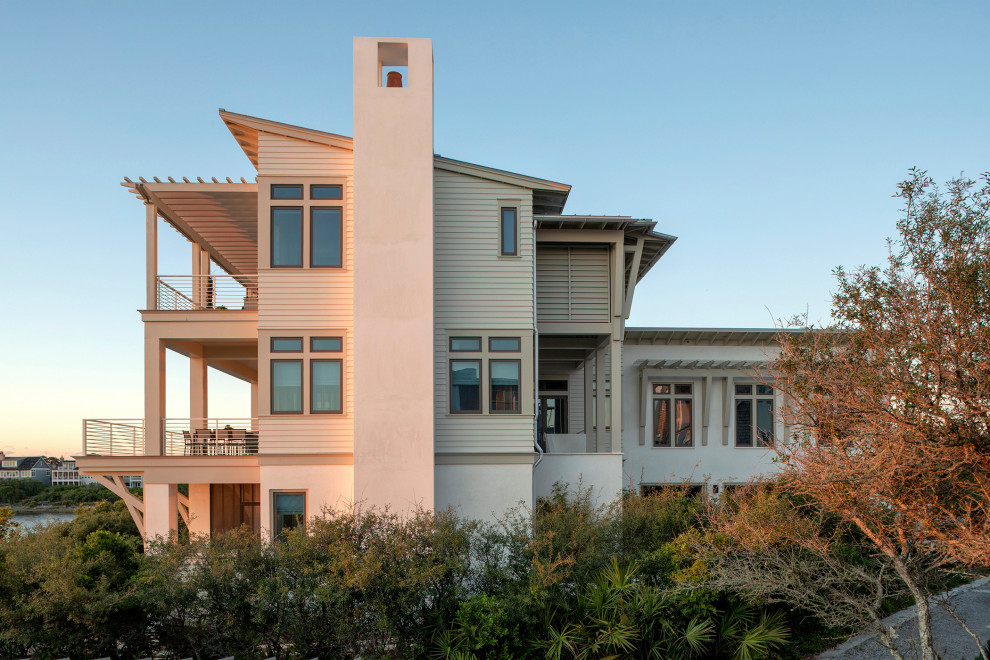 Idee per la facciata di una casa ampia beige stile marinaro a tre piani con rivestimenti misti, copertura in metallo o lamiera, tetto grigio, pannelli sovrapposti e terreno in pendenza
