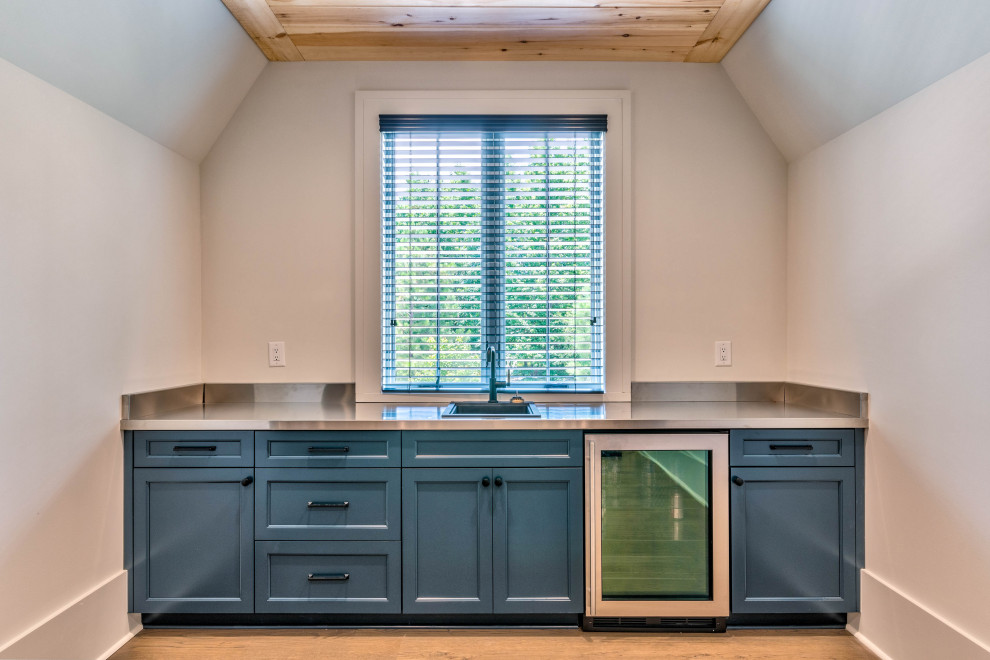 This is an example of a mid-sized modern single-wall wet bar in Atlanta with a drop-in sink, shaker cabinets, blue cabinets, stainless steel benchtops, grey splashback, medium hardwood floors and grey benchtop.