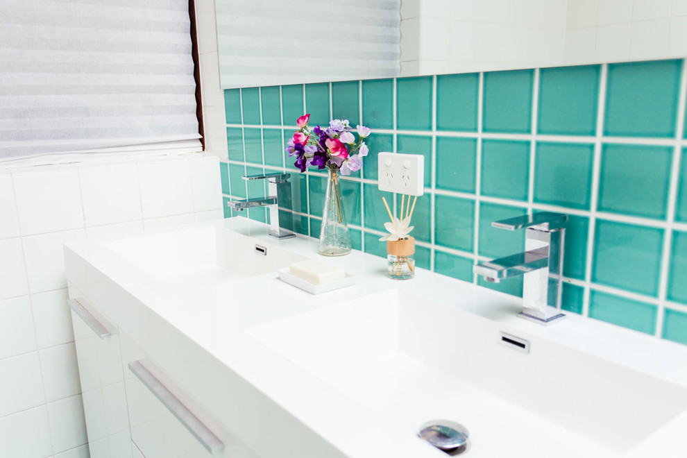 Mid-sized tropical 3/4 bathroom in Sydney with an integrated sink, beaded inset cabinets, white cabinets, solid surface benchtops, a corner tub, a corner shower, a wall-mount toilet, blue tile, glass tile, white walls and ceramic floors.