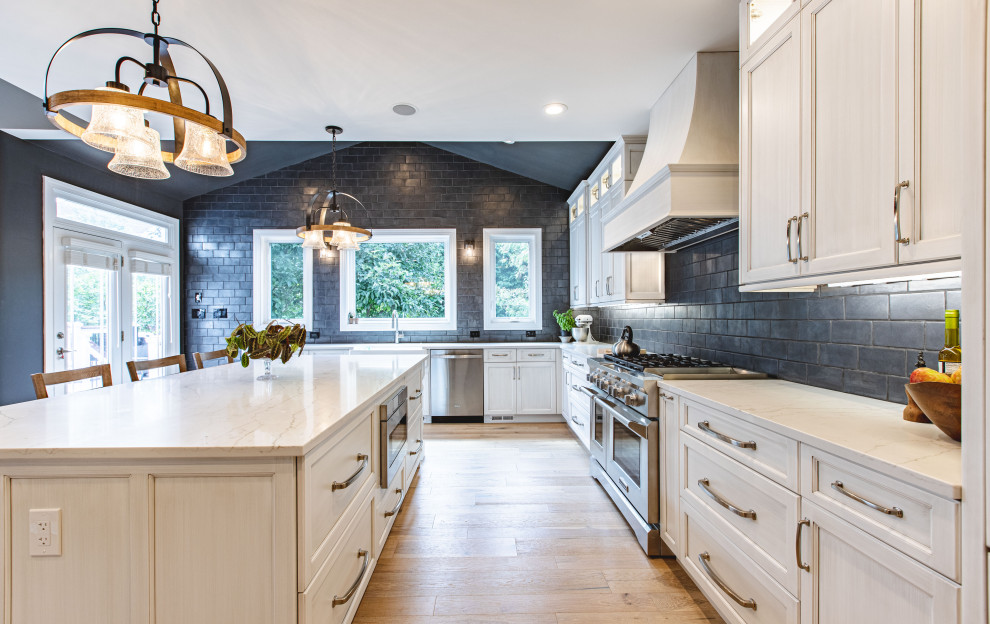 This is an example of a large traditional u-shaped separate kitchen in DC Metro with recessed-panel cabinets, light wood cabinets, marble benchtops, black splashback, subway tile splashback, panelled appliances, light hardwood floors, with island, beige floor and white benchtop.
