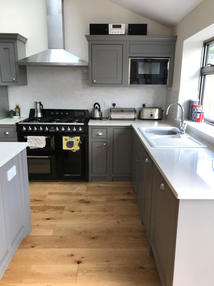 This is an example of a mid-sized traditional l-shaped kitchen in London with beaded inset cabinets, grey cabinets, quartzite benchtops, medium hardwood floors, with island, brown floor and white benchtop.