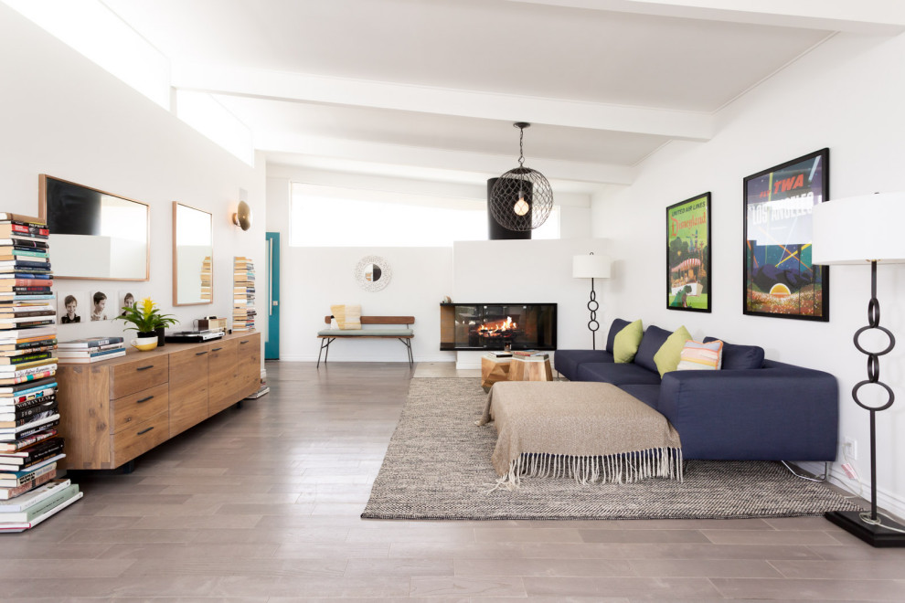 This is an example of a mid-sized midcentury open concept living room in Los Angeles with white walls, light hardwood floors, a corner fireplace, grey floor and exposed beam.