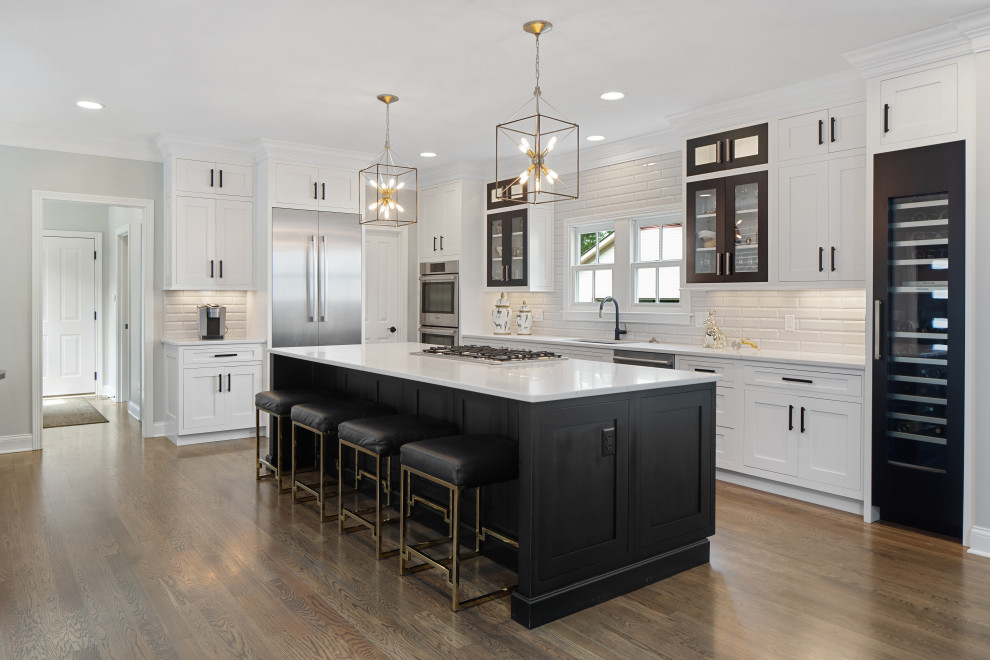 This is an example of a transitional l-shaped kitchen in Other with an undermount sink, shaker cabinets, white cabinets, white splashback, subway tile splashback, stainless steel appliances, dark hardwood floors, with island, brown floor and white benchtop.