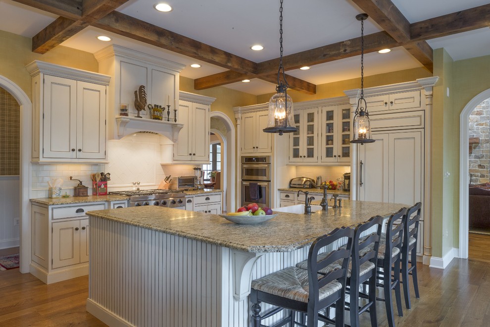 Design ideas for a country u-shaped kitchen in Other with a farmhouse sink, beaded inset cabinets, beige cabinets, white splashback, subway tile splashback, panelled appliances, medium hardwood floors, with island, brown floor and beige benchtop.