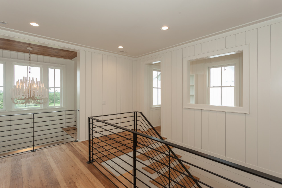 This is an example of a large beach style wood u-shaped staircase in Charleston with painted wood risers, metal railing and planked wall panelling.