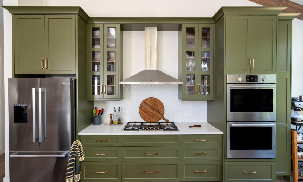 Mid-sized transitional l-shaped eat-in kitchen photo with an undermount sink, shaker cabinets, green cabinets, quartz countertops, white backsplash, ceramic backsplash, stainless steel appliances, an island and white countertops