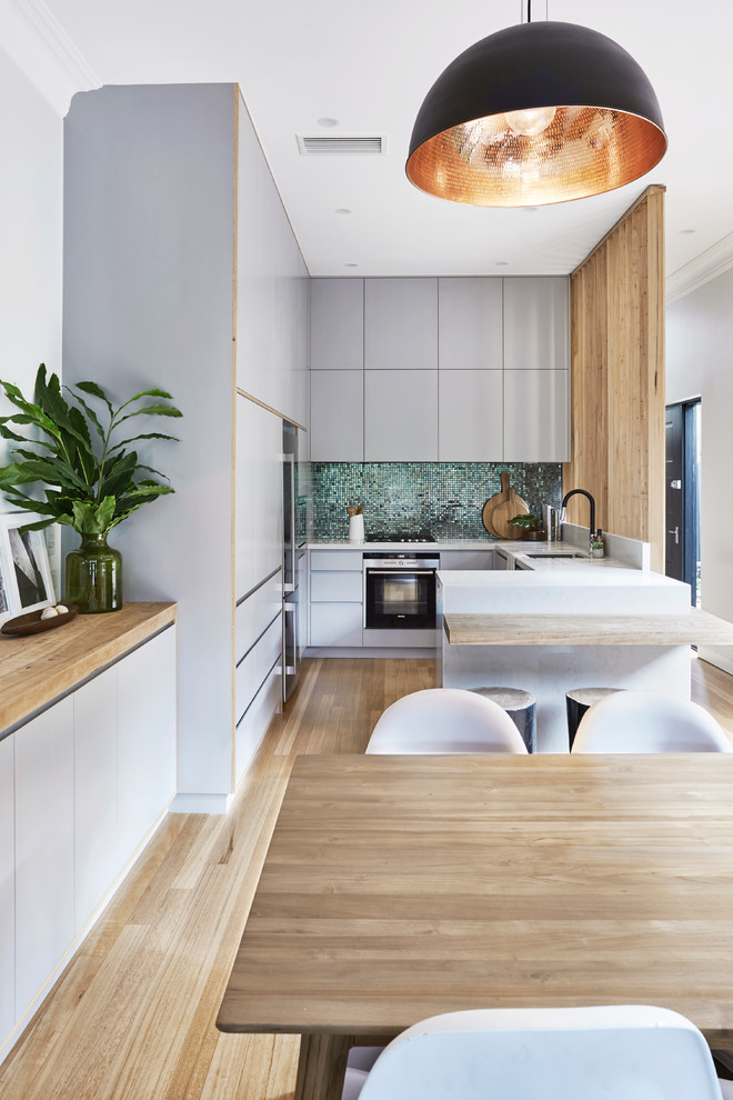 Mid-sized contemporary u-shaped kitchen in Sydney with an undermount sink, recessed-panel cabinets, blue cabinets, quartz benchtops, blue splashback, mosaic tile splashback, stainless steel appliances and light hardwood floors.
