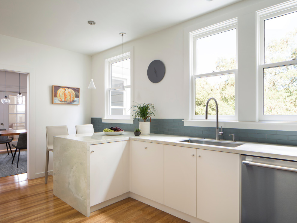 Photo of a mid-sized contemporary l-shaped eat-in kitchen in San Francisco with an undermount sink, flat-panel cabinets, white cabinets, marble benchtops, grey splashback, subway tile splashback, stainless steel appliances, medium hardwood floors, a peninsula, multi-coloured floor and white benchtop.