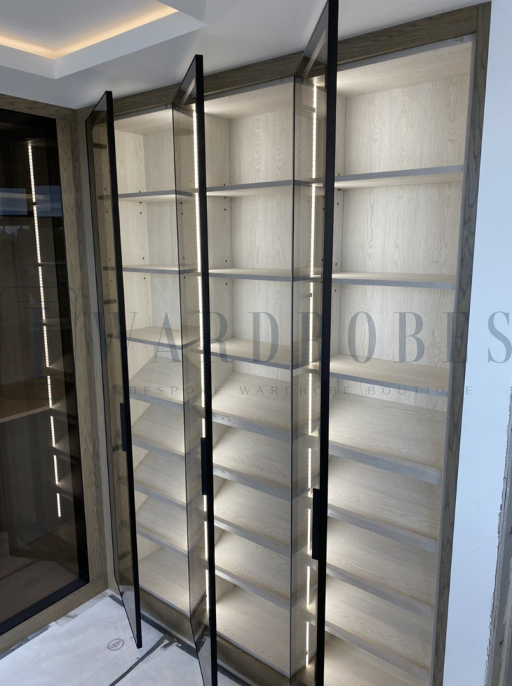 Photo of a large contemporary storage and wardrobe in London with glass-front cabinets and light wood cabinets.