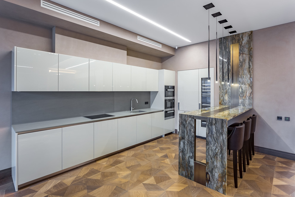Contemporary u-shaped open plan kitchen in Moscow with an undermount sink, flat-panel cabinets, white cabinets, grey splashback, stainless steel appliances, medium hardwood floors and a peninsula.