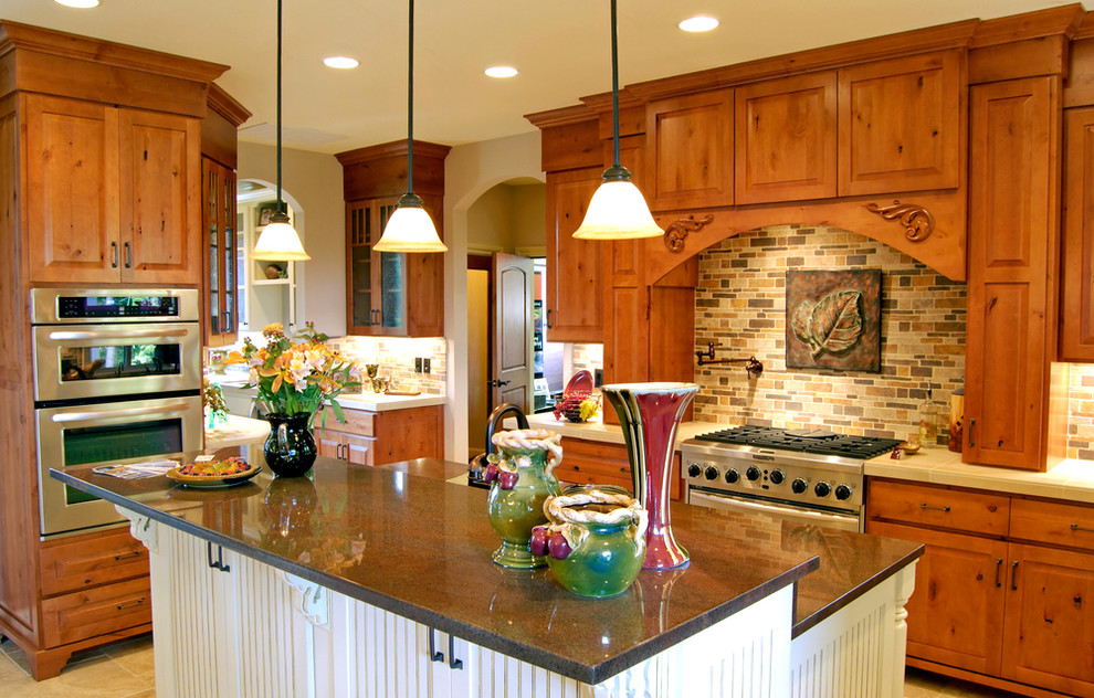 Mid-sized l-shaped travertine floor enclosed kitchen photo with a double-bowl sink, raised-panel cabinets, medium tone wood cabinets, granite countertops, brown backsplash, matchstick tile backsplash, stainless steel appliances and an island