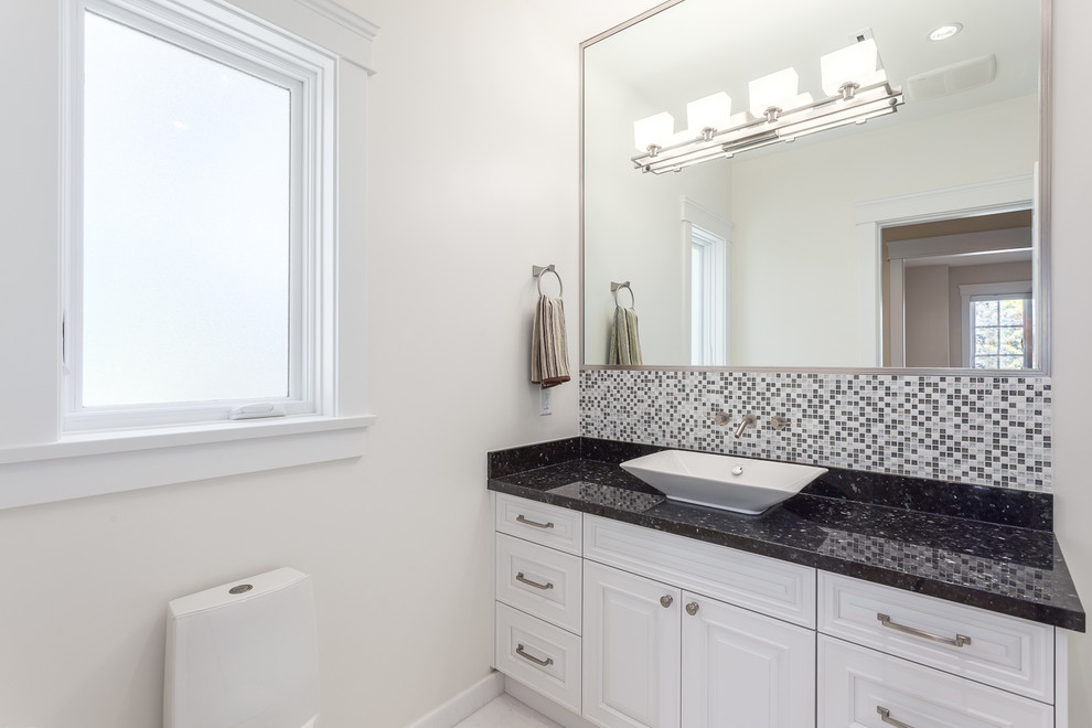 This is an example of a mid-sized contemporary powder room in Vancouver with white cabinets, a vessel sink, beaded inset cabinets, multi-coloured tile, mosaic tile, white walls, granite benchtops and black benchtops.