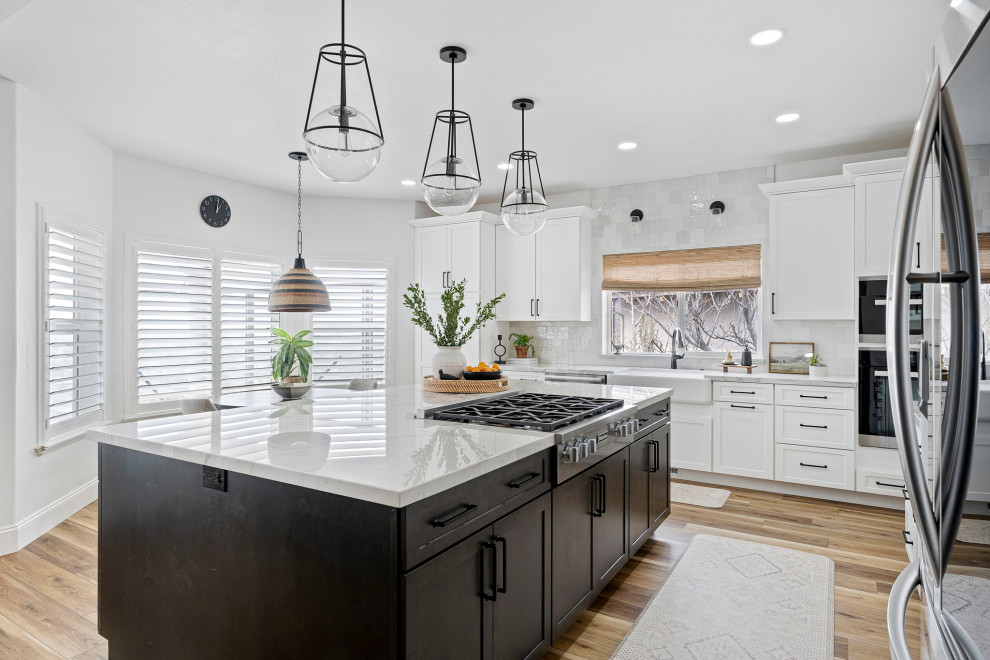 Example of a transitional vinyl floor and brown floor kitchen design with a farmhouse sink, shaker cabinets, white cabinets, quartzite countertops, white backsplash and stainless steel appliances