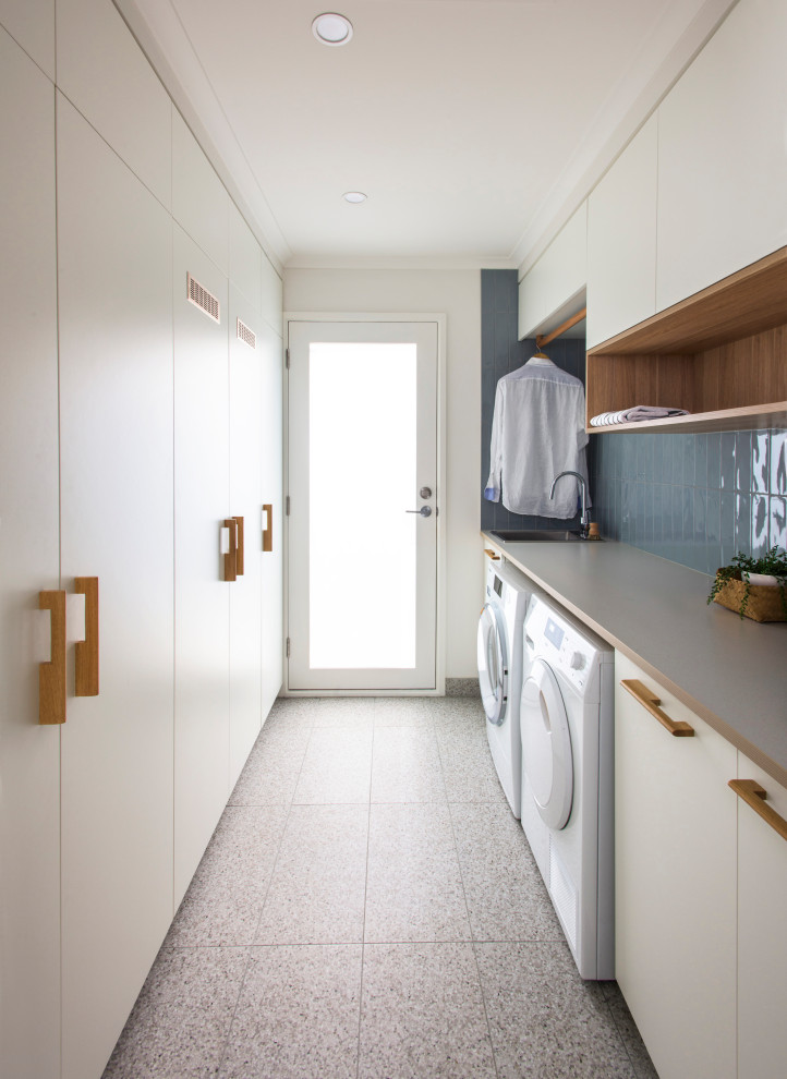 This is an example of a mid-sized contemporary galley laundry room in Melbourne with a single-bowl sink, white cabinets, laminate benchtops, blue splashback, subway tile splashback, porcelain floors, a side-by-side washer and dryer, grey floor and grey benchtop.
