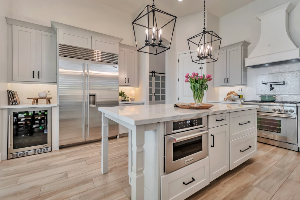 Inspiration for a large transitional u-shaped porcelain tile, brown floor and exposed beam kitchen remodel in Phoenix with a farmhouse sink, shaker cabinets, gray cabinets, quartzite countertops, white backsplash, porcelain backsplash, stainless steel appliances, an island and white countertops