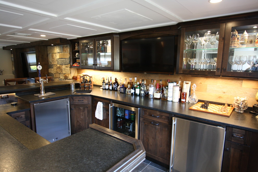Photo of a large traditional u-shaped seated home bar in New York with an undermount sink, glass-front cabinets, dark wood cabinets, granite benchtops, beige splashback, timber splashback, slate floors, multi-coloured floor and black benchtop.