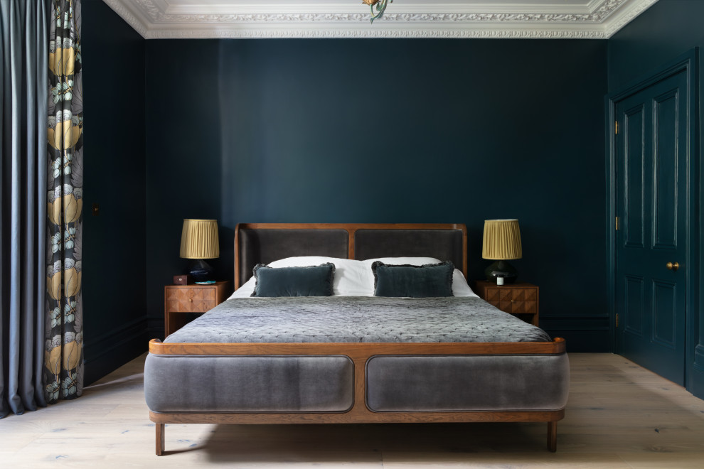 Modelo de dormitorio principal clásico renovado de tamaño medio con paredes azules, suelo de madera clara y marco de chimenea de metal