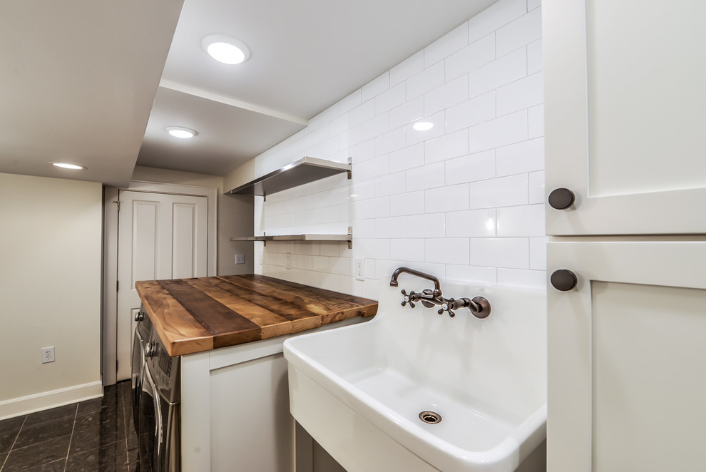 Photo of a mid-sized contemporary utility room in Cincinnati with an utility sink, shaker cabinets, white cabinets, wood benchtops, white walls, marble floors, a side-by-side washer and dryer, black floor and brown benchtop.