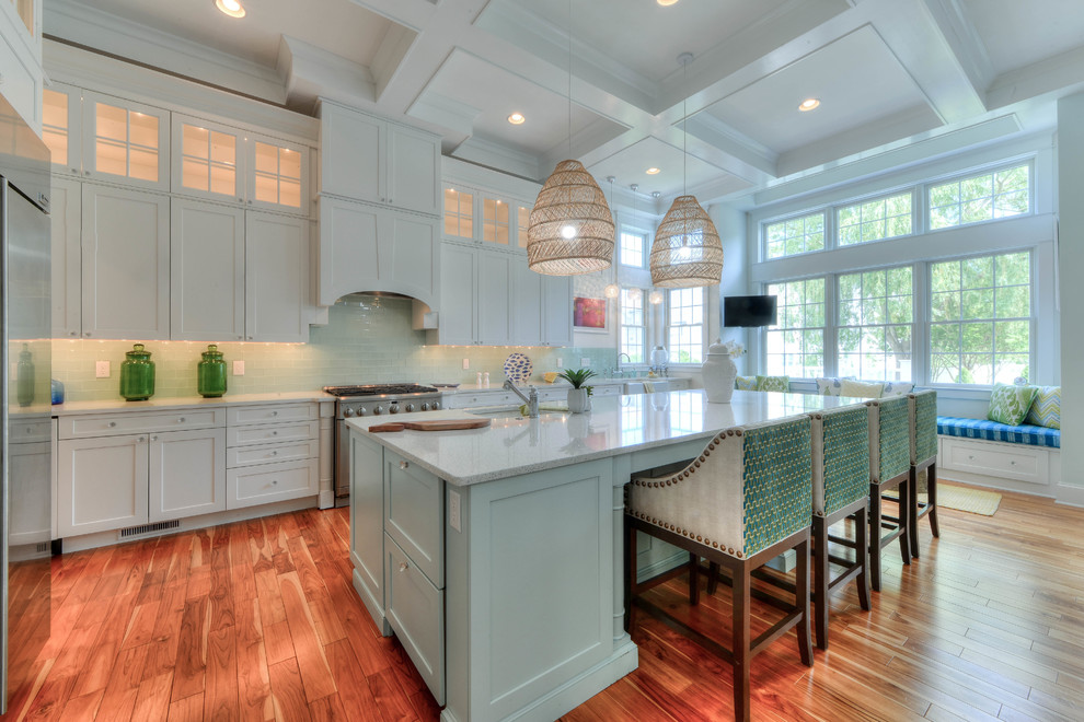 Design ideas for a beach style open plan kitchen in Philadelphia with an undermount sink, shaker cabinets, white cabinets, green splashback, glass tile splashback, stainless steel appliances, medium hardwood floors, with island, brown floor and white benchtop.