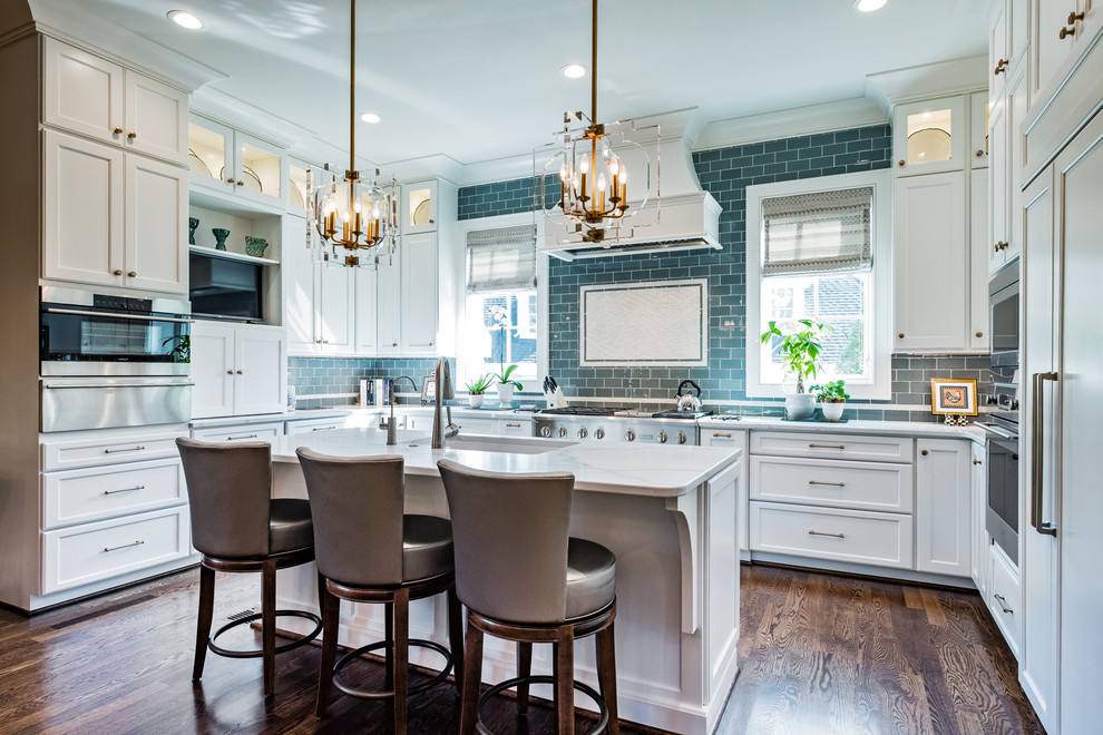 Example of a large transitional u-shaped dark wood floor and brown floor kitchen design with an undermount sink, shaker cabinets, white cabinets, marble countertops, blue backsplash, subway tile backsplash, stainless steel appliances and an island