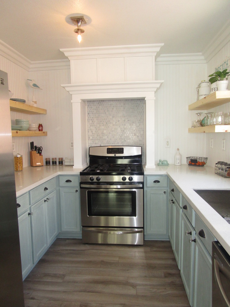 Photo of a small beach style u-shaped kitchen in Other with a single-bowl sink, blue cabinets, quartz benchtops, grey splashback, stainless steel appliances and light hardwood floors.