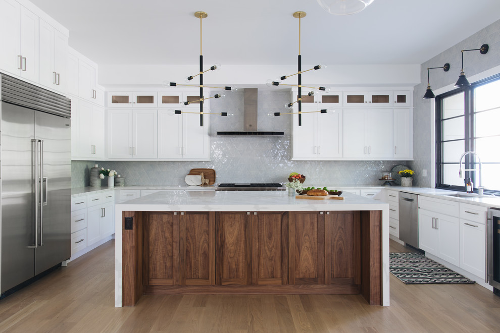 Inspiration for a transitional u-shaped kitchen in Chicago with an undermount sink, shaker cabinets, white cabinets, grey splashback, stainless steel appliances, medium hardwood floors, with island, brown floor and white benchtop.