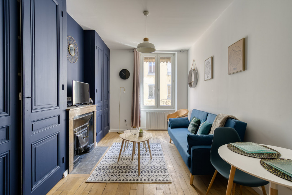 Esempio di un piccolo soggiorno minimalista aperto con pareti blu, parquet chiaro, camino classico, cornice del camino in pietra ricostruita e TV autoportante