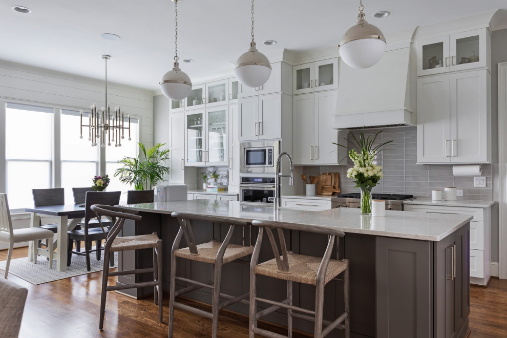 Example of a mid-sized transitional single-wall light wood floor and brown floor kitchen design in Raleigh with glass-front cabinets, white cabinets, gray backsplash, glass tile backsplash, stainless steel appliances, an island and white countertops