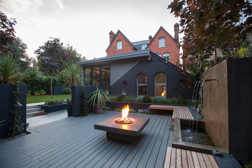 Large contemporary backyard deck in Hampshire with a fire feature.