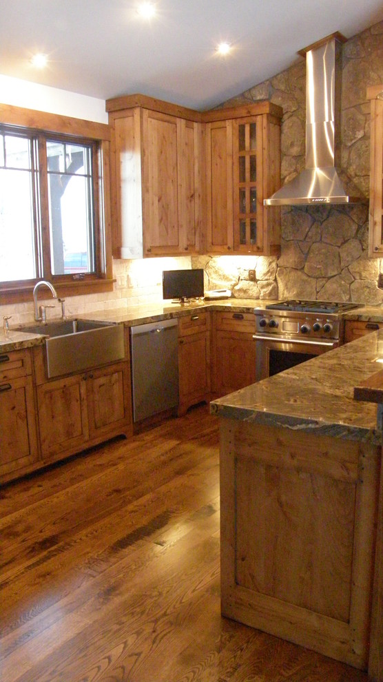 Example of a large mountain style l-shaped medium tone wood floor, brown floor and vaulted ceiling eat-in kitchen design with a farmhouse sink, raised-panel cabinets, medium tone wood cabinets, granite countertops, gray backsplash, stone tile backsplash, stainless steel appliances, an island and gray countertops